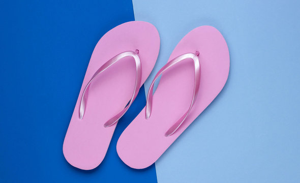 Fashionable beach pink flip flops on blue paper background. Top view