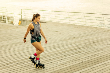 Young attractive sport woman roller skating on the beach