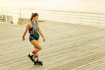 Young attractive sport woman roller skating on the beach