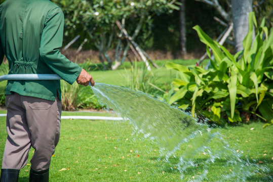 Man watering the garden with hose in the backyard