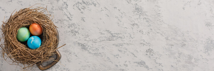 Easter eggs in a bird's nest on a textural background. Easter celebration concept. Copy space. Flat lay. Banner.