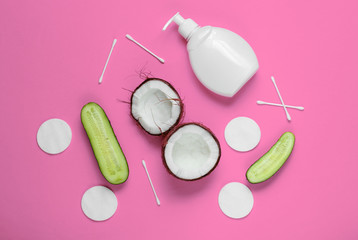 Natural cosmetics, skin care products. Coconut, cucumbers, bottle of cream, cosmetic accessories on pink background. Top view. Minimalistic beauty concept. Flat lay style