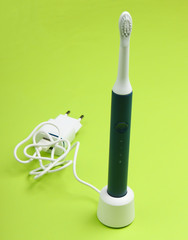 Modern electric toothbrush with a charger on a green background.