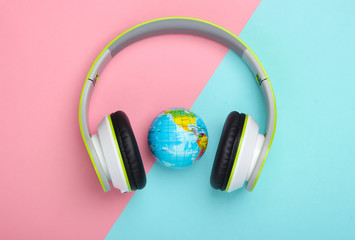 World song. Global music chart. The music of earth. Stereo headphones and a globe on a blue-pink pastel background. Top view