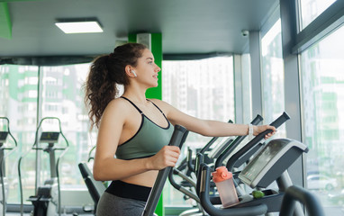 Young attractive woman warming up on an elliptical exercise machine in the gym. Fitness, healthy...