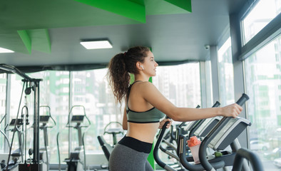 Fototapeta premium Young attractive woman warming up on an elliptical exercise machine in the gym. Fitness, healthy lifestyle concept.