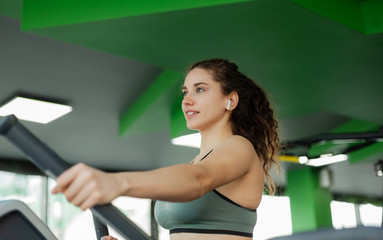 Young attractive woman is exercising on elliptical exercise machine in the gym. Fitness, healthy lifestyle concept.
