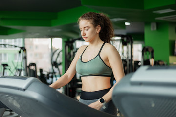 Fototapeta na wymiar Young fit woman in sportswear before basic training runs on a treadmill in the gym. The concept of a healthy lifestyle, warming up, fitness.