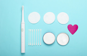 Flat lay composition of hygiene products. Toothbrush, cotton pads, ear sticks, cream on a blue background. Top view