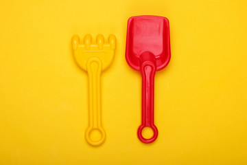 Children's rake and shovel for a sandbox or beach on a yellow studio background. Top view