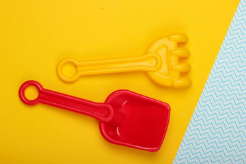 Children's rake and shovel for a sandbox or beach on yellow blue studio background. Top view