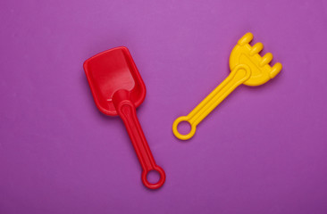 Children's rake and shovel for a sandbox or beach on purple studio background. Top view