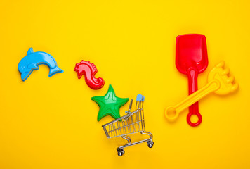 Children's beach toys or sandbox toys and shopping trolley on yellow background. Top view