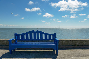 Blue wooden bench against the sea and yacht on the horizon.
