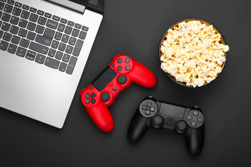 Laptop, Two gamepads and a bowl of popcorn on black background. Gaming, leisure and entertainment concept. Top view