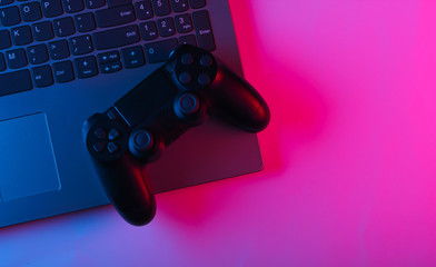 Laptop and gamepads with blue pink neon vibrant light. Gaming, leisure and entertainment concept. Top view