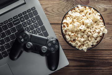 Laptop, gamepad and bowl of popcorn on wooden table. Gaming, leisure and entertainment concept. Top view © splitov27