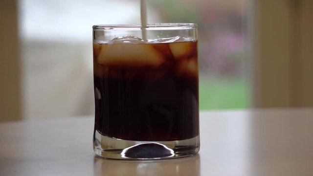 pouring milk iinto a short glass of cold brew coffee