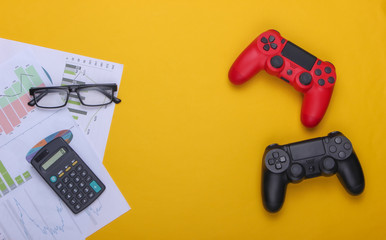 Entertainment or work. Gamepads, charts and diagrams, glasses and calculator on yellow background. Versus. Top view © splitov27
