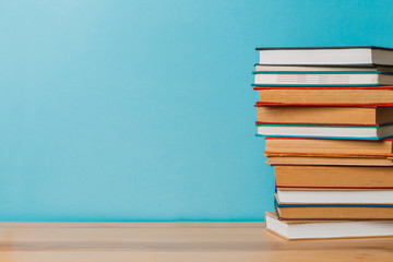 A simple composition of many hardback books, raw books on a wooden table and a bright blue background. Going back to school. Copy space. Education.