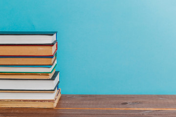 A simple composition of many hardback books, raw books on a wooden table and a bright blue background. Going back to school. Copy space. Education.