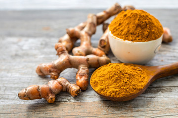Turmeric (curcumin) powder and fresh rhizome on a wooden background.