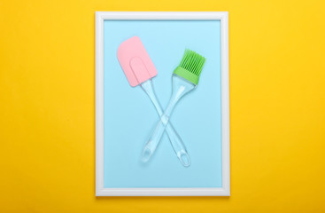 Kitchen spatula and brush on yellow background with photo frame. Studio shot. Creative flat lay. Top view. Minimalism