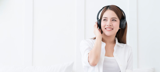 banner attractive asian Happy young woman in earphones is listening to music with smart phone, relax on bed, singing and smiling with white bedroom interior background freedom lifestyle activity