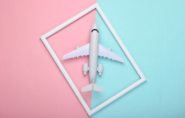 Airplane in a white frame on pink blue pastel background. Travel concept. Top view. Flat lay