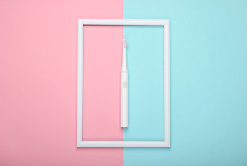 Electric toothbrush on pink blue pastel background with white frame. Studio shot. Creative flat lay. Top view. Minimalism
