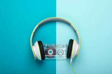 Stylish wired stereo headphones with audio cassette on blue background. Music lover. Retro 80s. Top view.