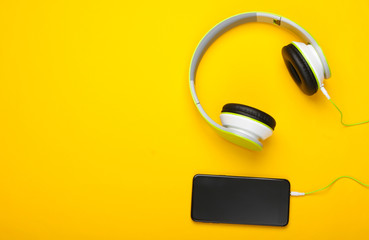 Stylish wired stereo headphones with smartphone on yellow background. Music lover. Modern gadgets. Top view. Minimalism