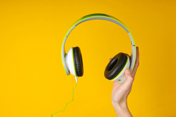 Hand holding stereo headphones on a yellow background.