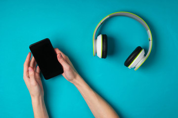 Female hands hold the phone and synchronize the headphones on a blue background. Modern gadgets....