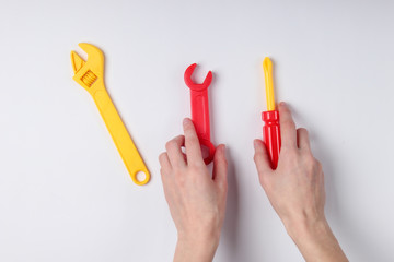 Hands holding a toy screwdriver and wrench on white background.