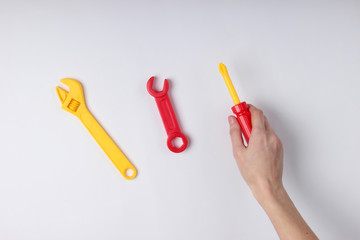 Hands holding a toy screwdriver and wrench on white background. Top view