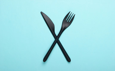 Black plastic knife with a fork on a blue background. Top view. Minimalism