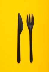 Black plastic knife with a fork on yellow background. Top view. Minimalism