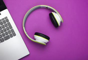 Laptop with headphones on purple background. DJ, gaming, entertainment or leisure concept. Top view. Flat lay