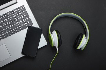 Laptop with stereo headphones and smartphone on black background. Flat lay composition. Modern gadgets. Top view