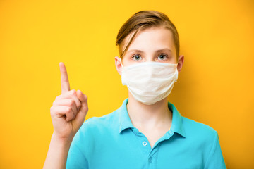 Young teen boy wearing health mask shows the index finger up against yellow background. Healthcare information about corona virus concept. Novel Coronavirus