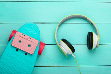 Flat lay hipster composition. Cruiser board, audio cassette, headphones on blue wooden background. Retro 80s entertainments. Summer fun. Top view
