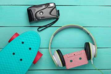 Flat lay hipster composition. Cruiser board, audio cassette, headphones, camera on blue wooden background. Retro 80s entertainments. Summer fun. Top view