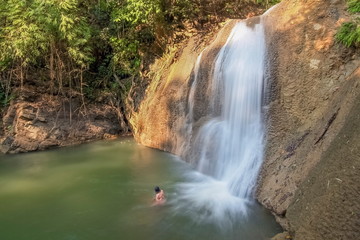 Fototapeta premium view of silky waterfall flowing from rock cliff around with green forest background, Nang Kruan Waterfall, Lam Klong Ngu National Park, Kanchanaburi, west of Thailand.