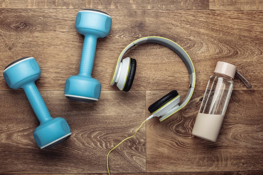 Flat lay sports and fitness composition, training. Dumbbells and headphones, water bottle on wooden floor. Top view
