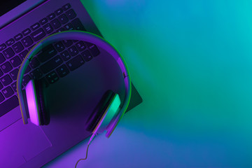 Laptop and headphones with neon green purple light. Gradient glow. Gaming or DJ concept. Top view