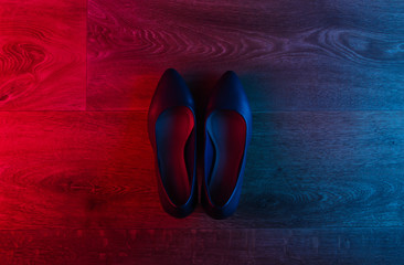 Leather high heel shoes on wooden floor with neon red-blue gradient glow. Top view