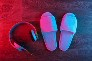 White slippers with headphones on wooden floor with neon red-blue gradient glow. Insomnia. Top view