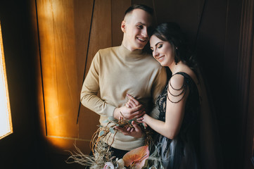 Beautiful bride and groom with a wreath of flowers are hugging in a vintage interior near a wooden...