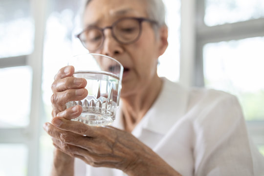 Senior woman holding glass of water,hand shaking while drinking water,elderly patient with hands tremor uncontrolled body tremors,symptom of essential tremor,parkinson's disease,neurological disorders